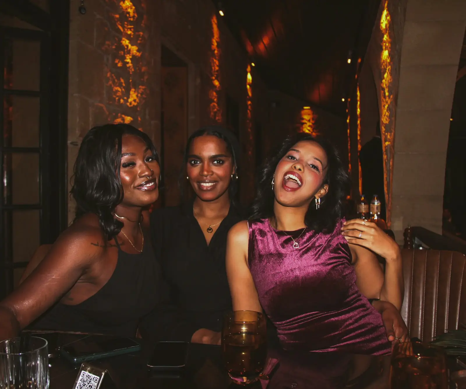 Three friends laughing at a table in a dark bar